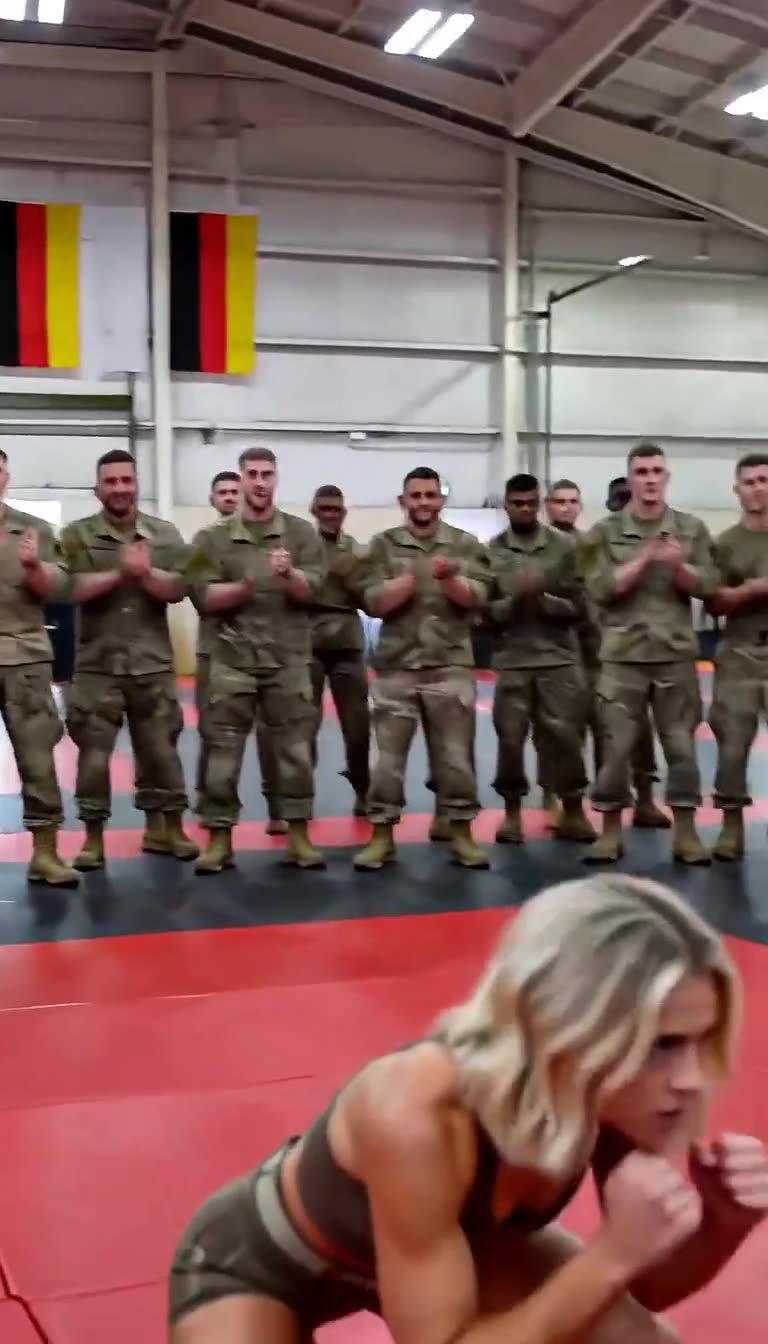 Onlooking soldiers applaud as the female fighter ducks into a combat stance