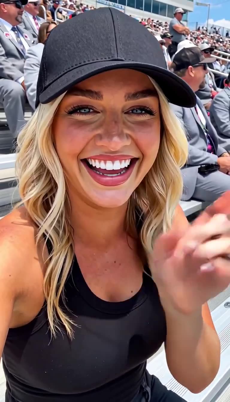 Chloe laughing with broad delight and waving her hand in front of the packed stadium grandstand.