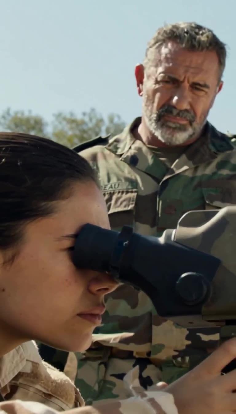 Nora remains focused on her target through the optic as Moreau observes closely