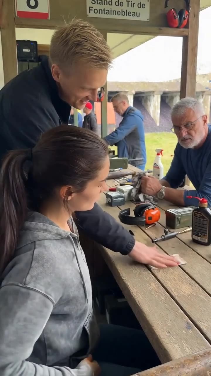 Maxime slapping euro banknotes onto the wooden firing bench as an older shooter stops to watch.