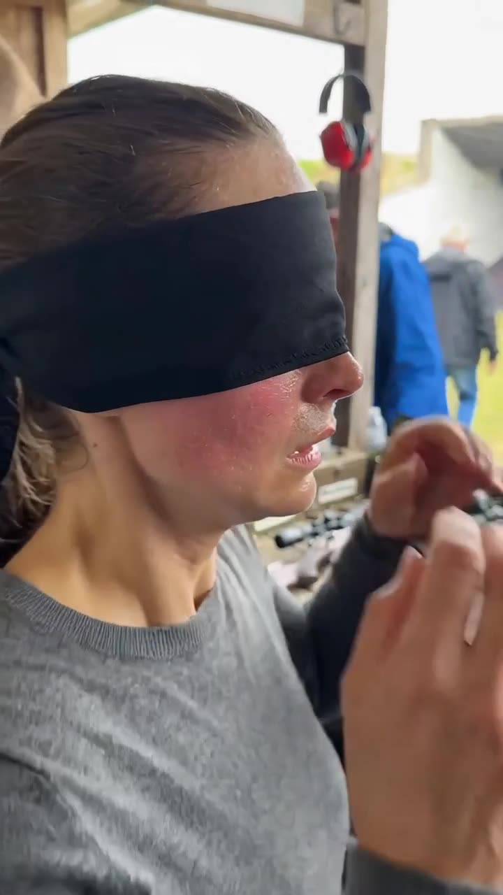 Close-up profile of the woman preparing to shoot while wearing a tight black blindfold.