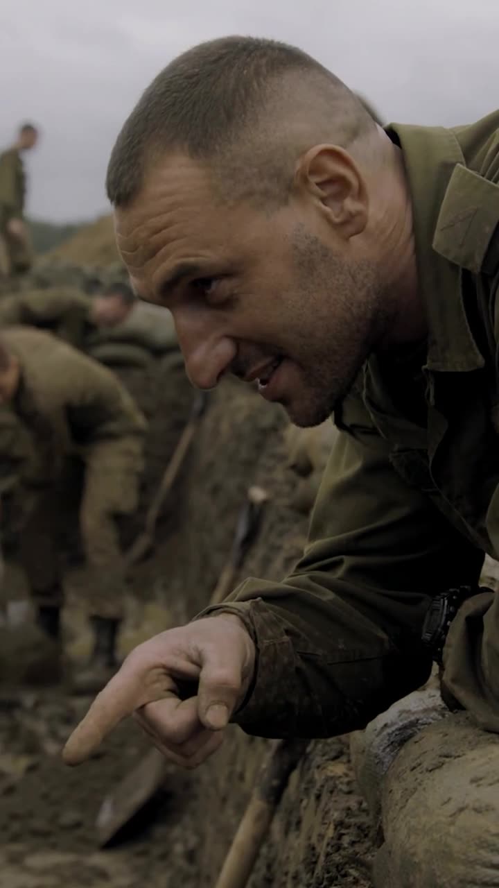 Julien leans over the trench rim with a grin, pointing mockingly down into the mud.