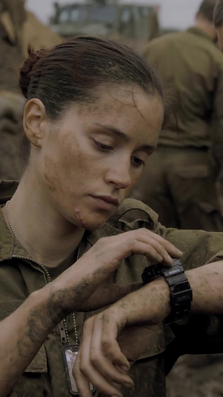 Camille calmly raises her wrist to inspect her black digital watch, revealing a steel chain beneath her collar.