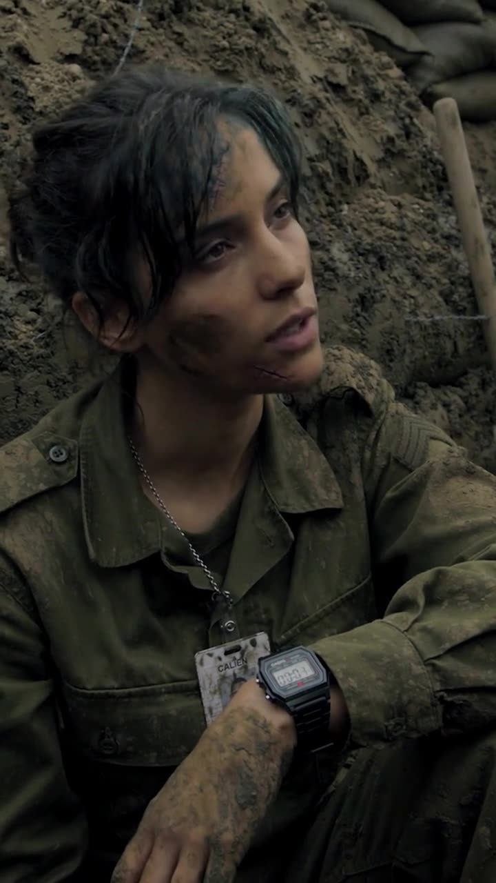 Camille sitting calmly in the trench wearing a digital watch displaying the final seconds