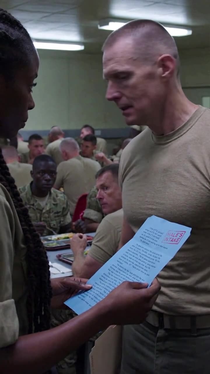 Maya holds up the blue carbon intake form with a red stamp as Derek stares nervously in the dining hall.