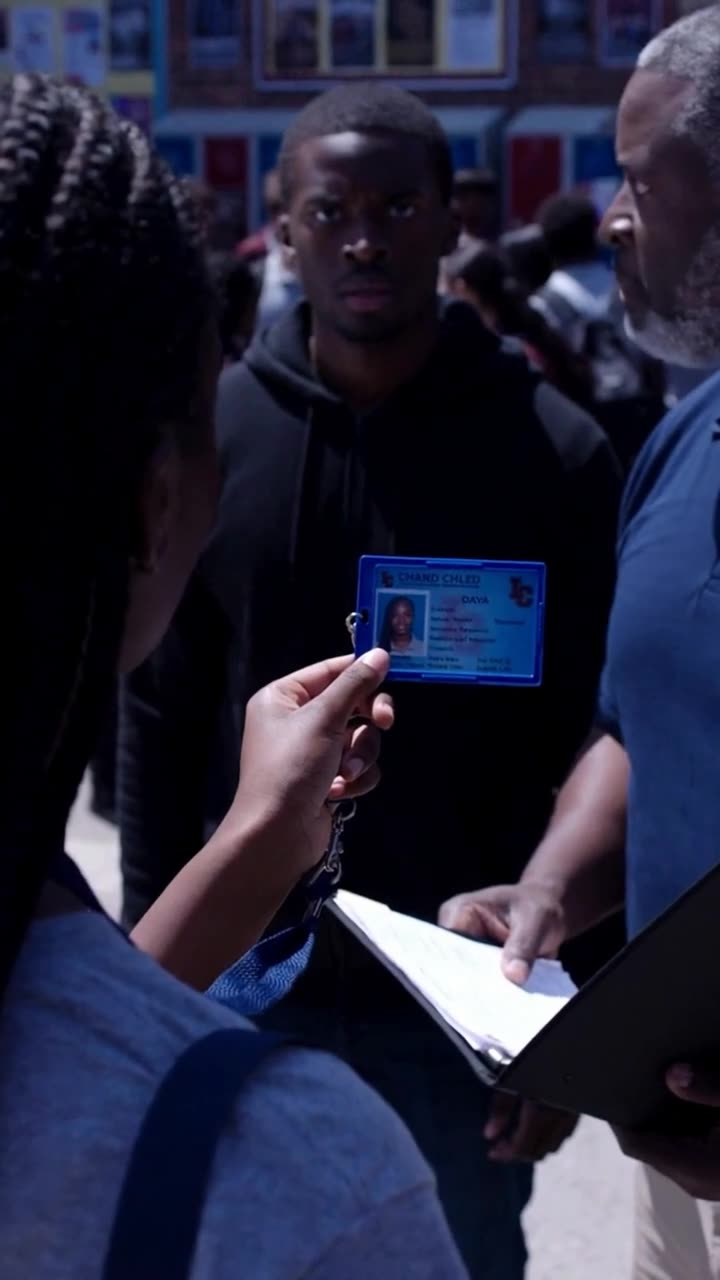 Maya presenting an official blue identification badge held between her fingers.
