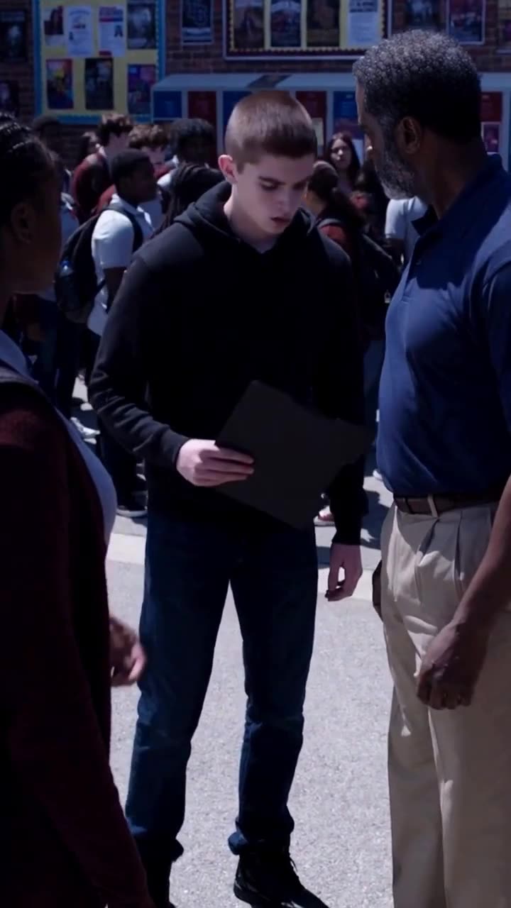 A defeated male student looks down at a disciplinary clipboard in front of an administrator.
