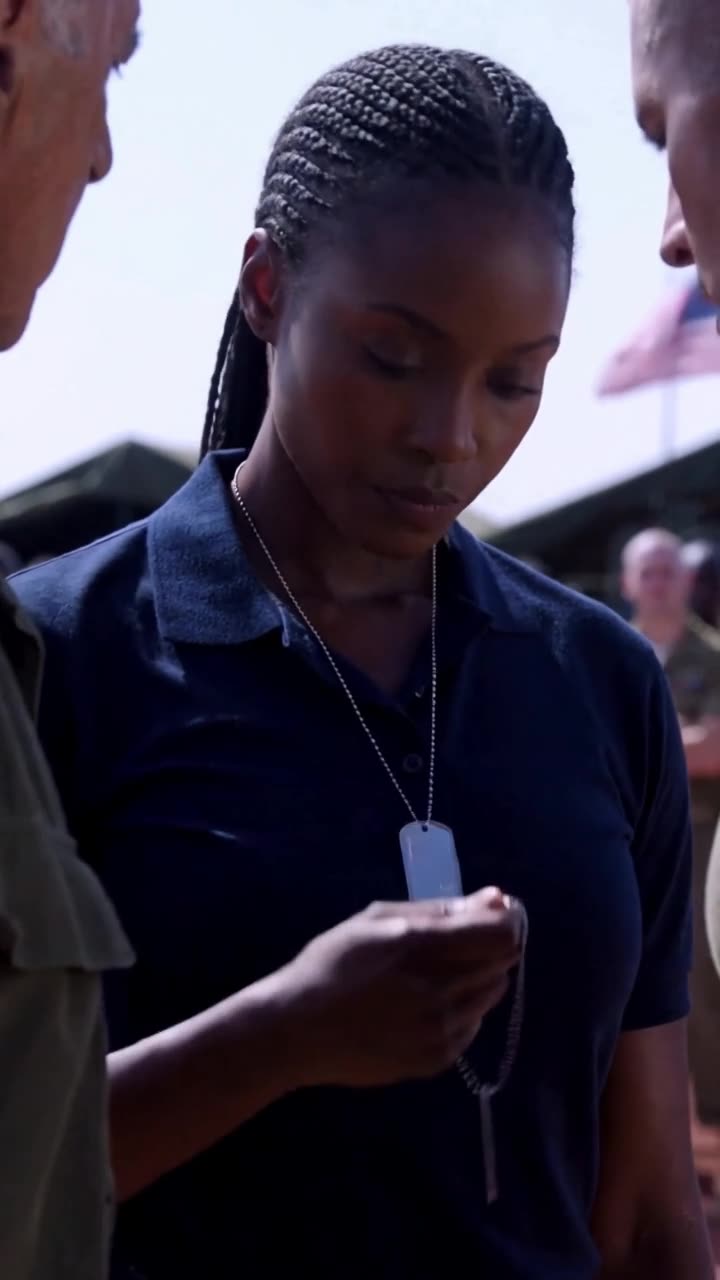 Maya lowers her gaze as she unclasps the steel dog tags in front of the base commanders.