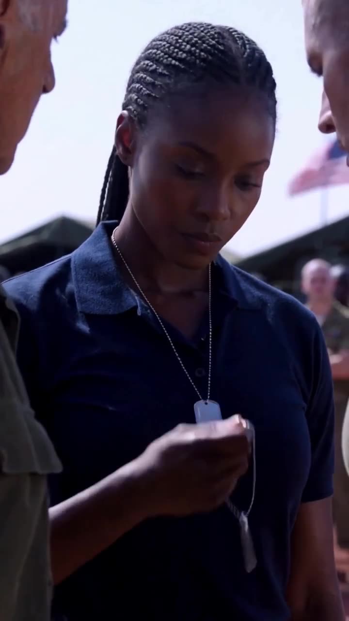 The female commander looks down at her dog tags with steady, focused composure.