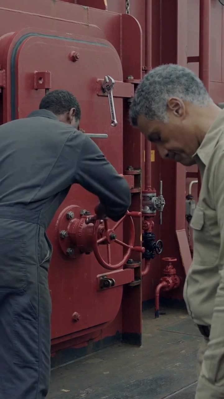 Thomas turning the dog valve on the sealed red bulkhead hatch as Vance drops his head against the railing in defeat.