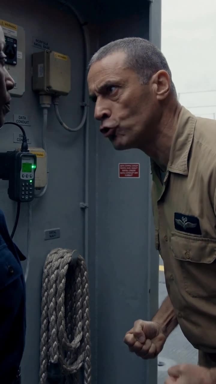 Kane clenches his fists and shouts furiously beside the flashing green transponder conduit.