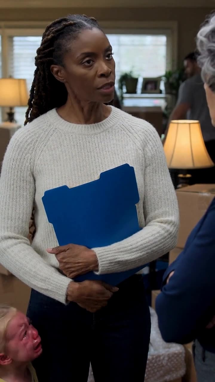 Kendra firmly clutches the blue deed folder to her chest, holding her ground in the sunroom.