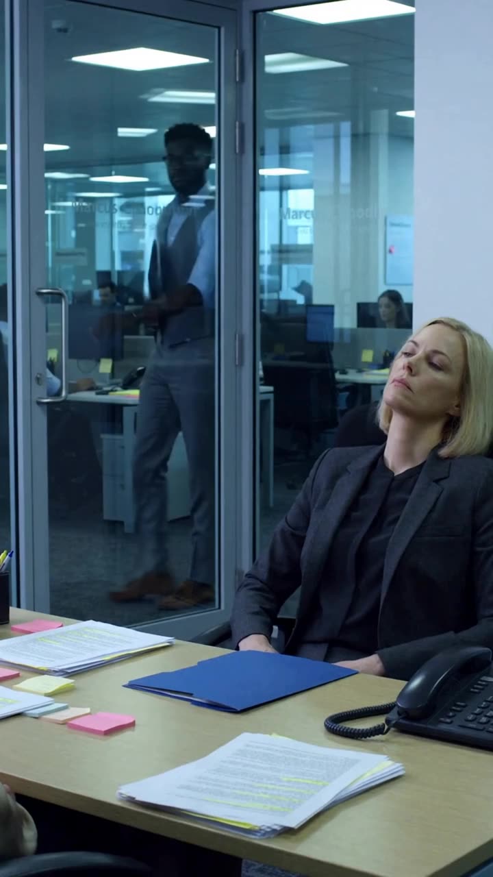 Evelyn leans back coldly in her chair as Marcus is seen outside the glass door.