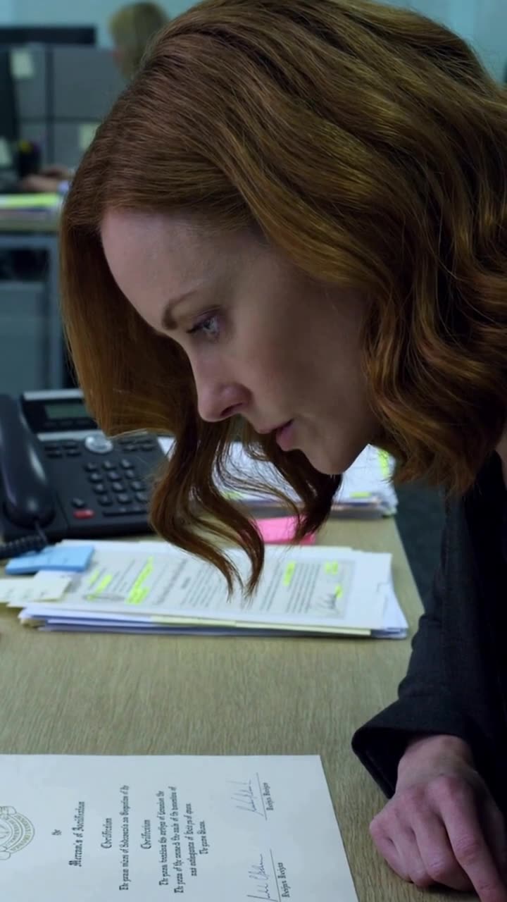 Chloe glances down in defeat at the formal review documents spread across her desk.