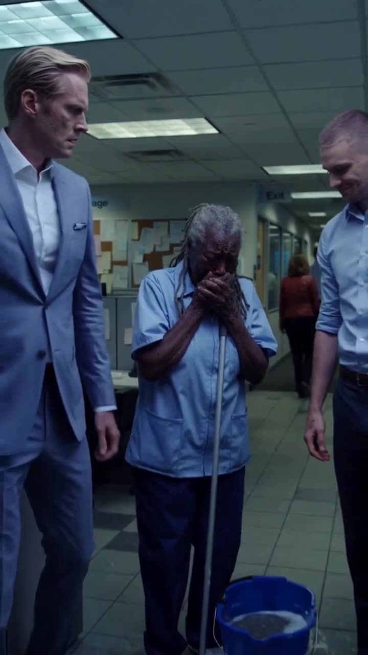 The CEO stands sternly in a suit as the elderly janitor weeps into her hands