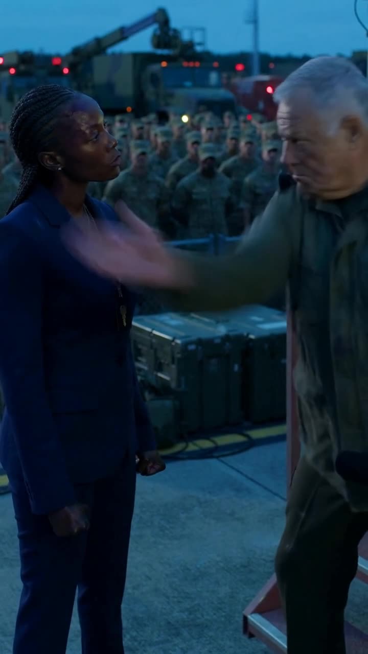 Thomas gestures dismissively with his hand as Maya stands resolute before the gathered troops