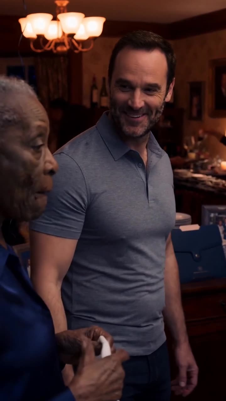 Mark casts a mocking smile toward Evelyn as the navy document folder sits on the sideboard.
