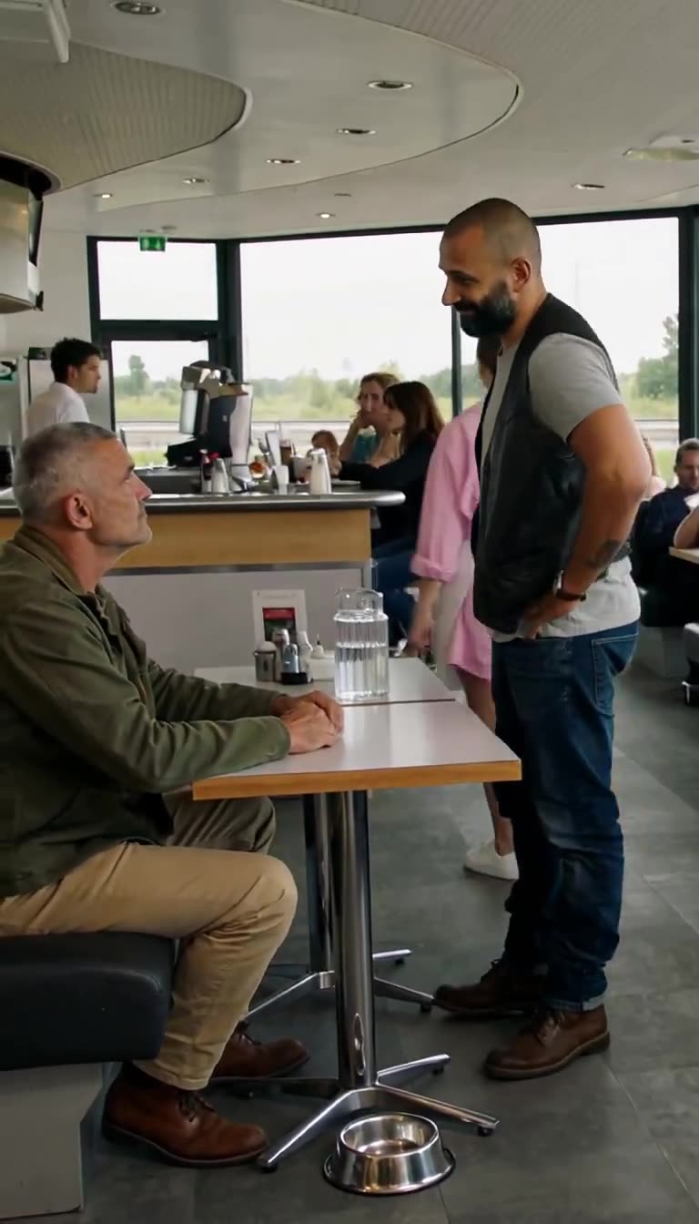 Julien stares coldly up at Franck as the power balance shifts across the roadside booth.