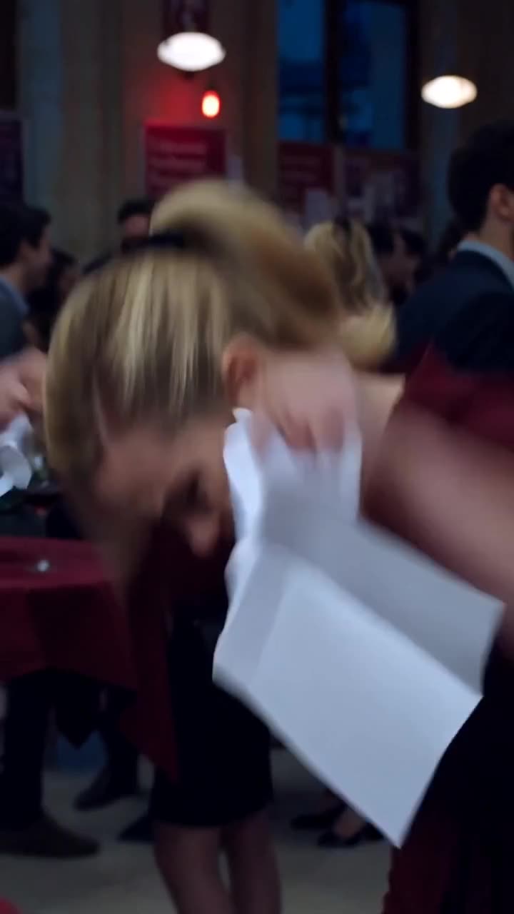 A blonde woman in a burgundy dress violently tears up the employment paper in front of guests.