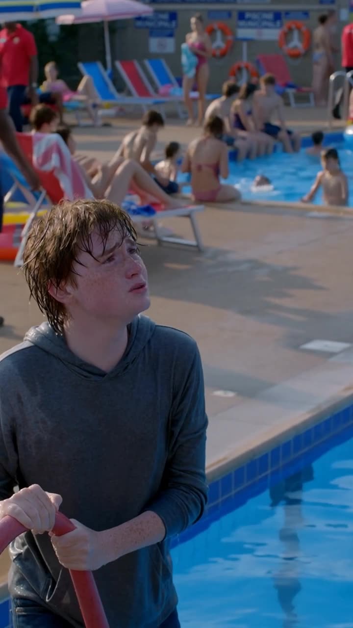 Julien grips the pool railing and looks up pleadingly at Lucas