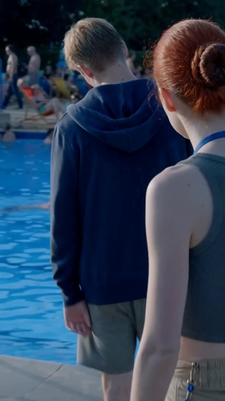 The red-haired girl stands resolutely behind the bully near the water right before the confrontation.