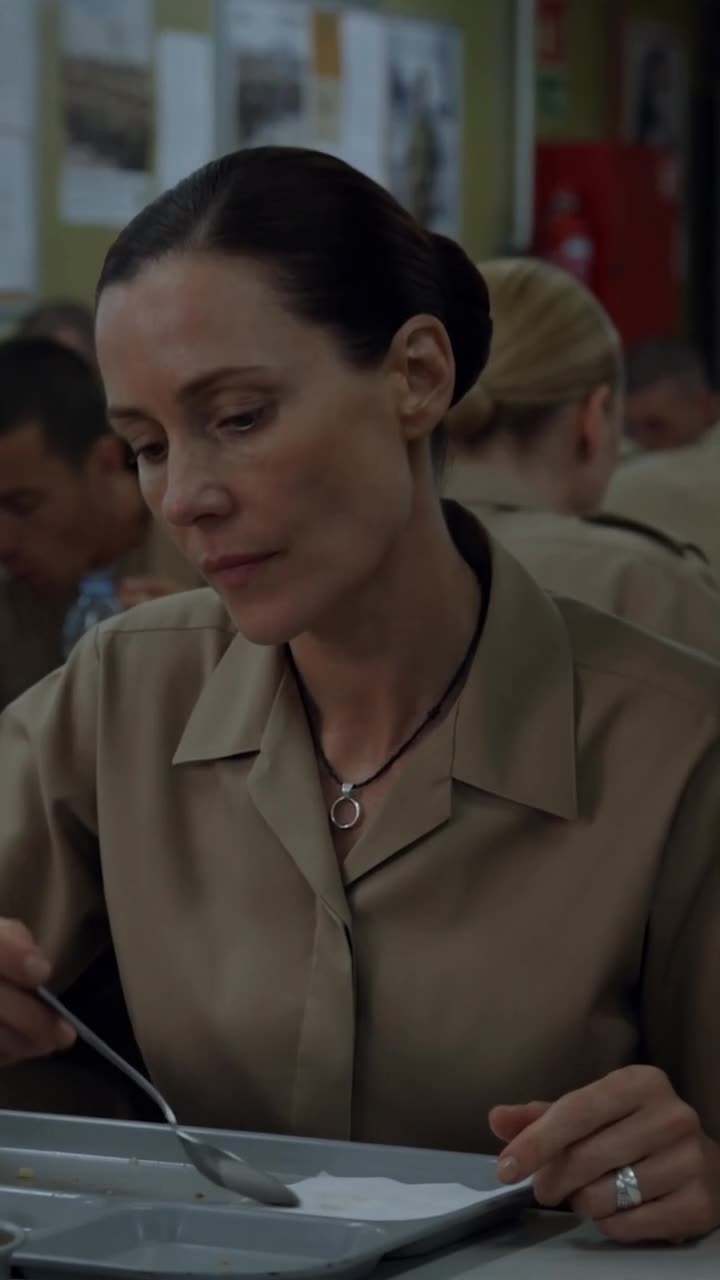 Claire calmly lowering her spoon as a silver signet ring shows beneath her open collar
