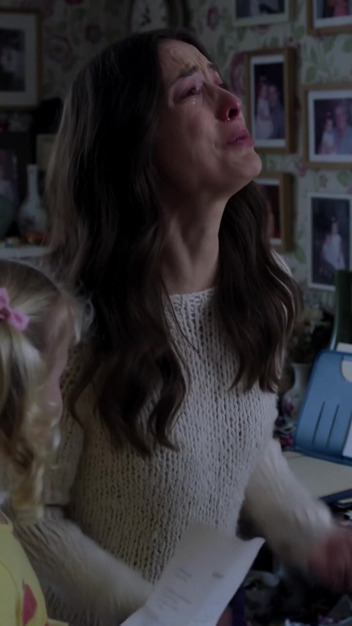 A weeping Camille tilts her head up in tears while grasping the legal document of ownership.