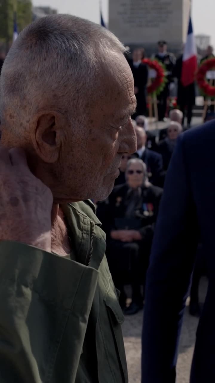 Henri reaches his hand up toward his neck, preparing to reveal a hidden cord under his jacket collar