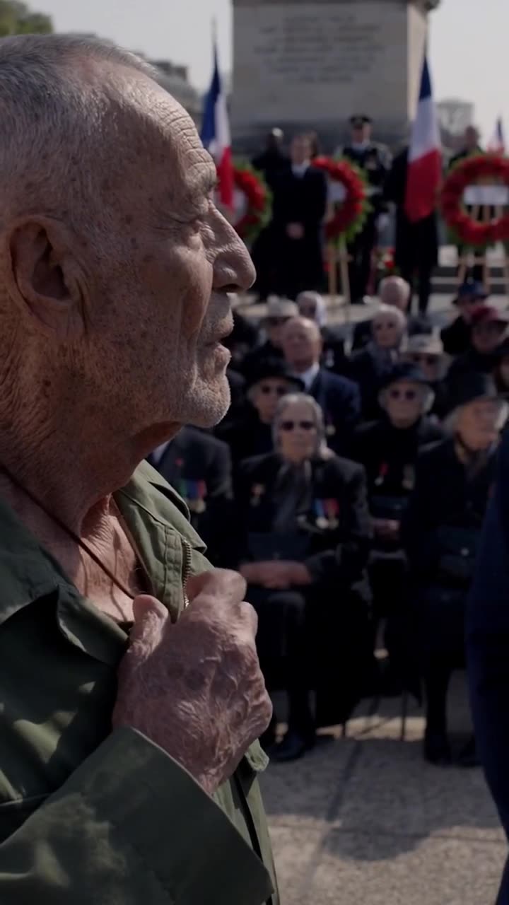 Close-up of the weathered veteran clutching his jacket with stoic resolve in front of seated dignitaries
