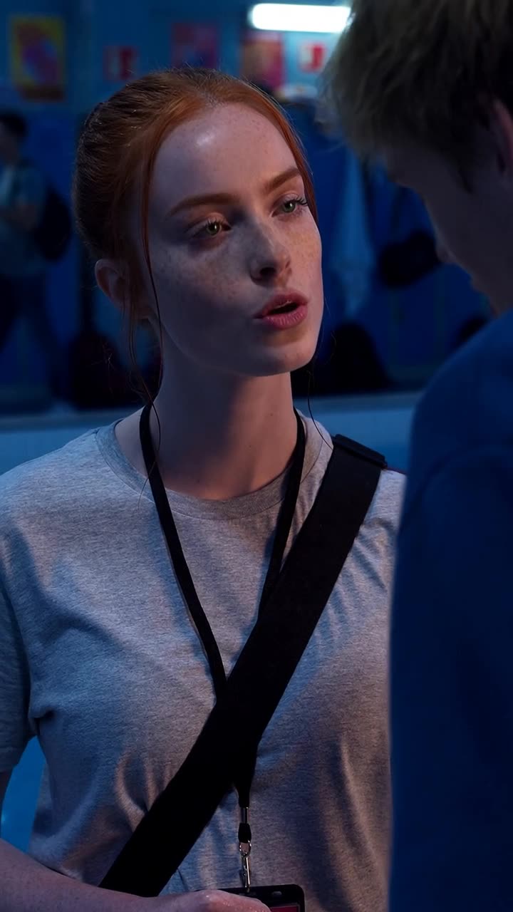 Camille looks upward with calm defiance, wearing a lanyard while addressing Maxime at dusk.