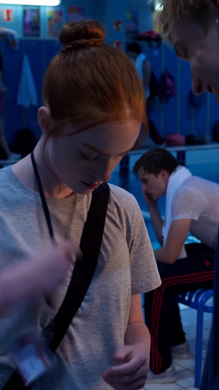 Camille looks down calmly while reaching beneath her collar for a hidden lanyard