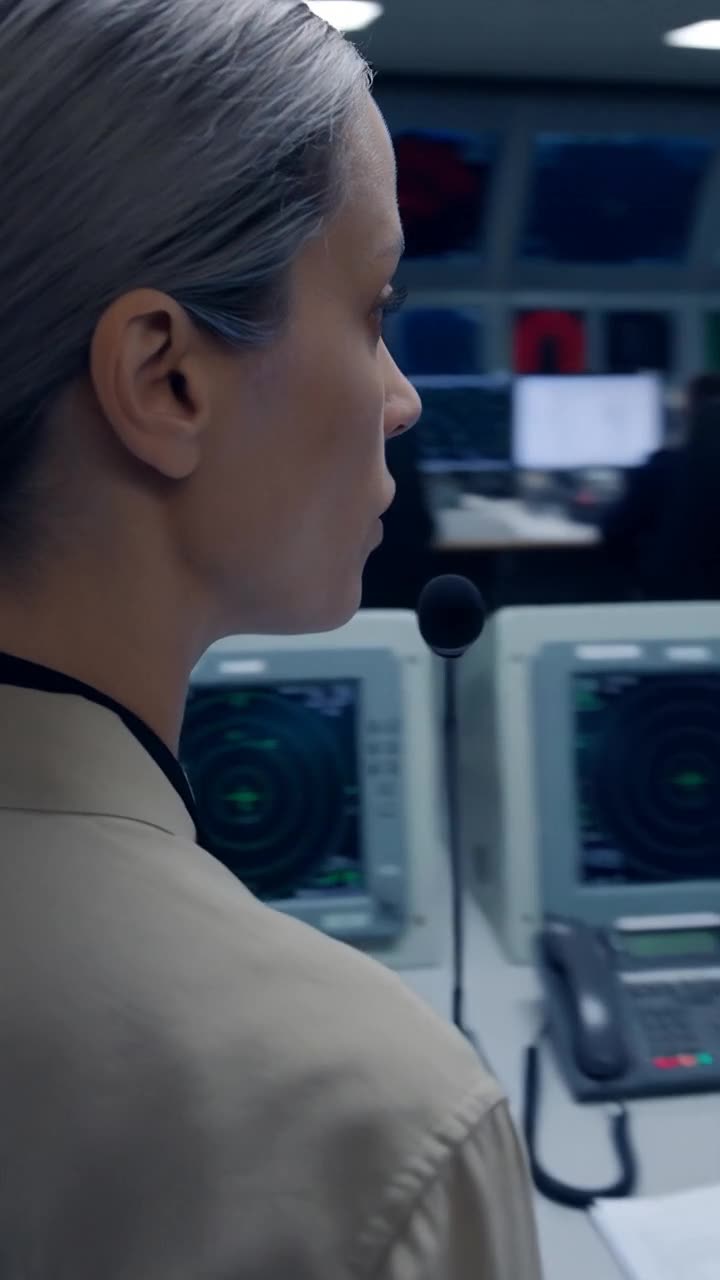 Camille speaks steadily into the operations desk microphone in profile.