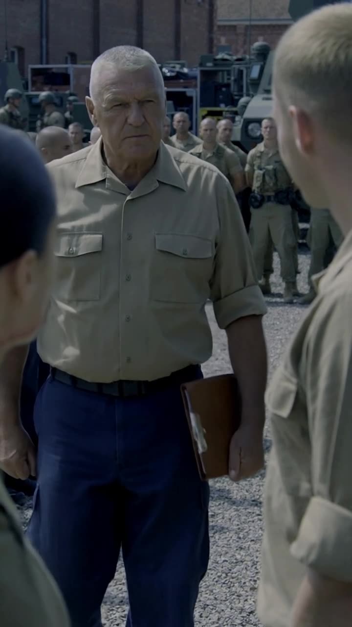 Commander Philippe strides into the center of the yard holding a clipboard and barking orders.