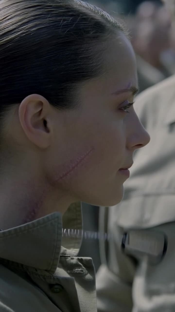 Close profile of Camille showing her scarred jawline as the wind shifts her collar.