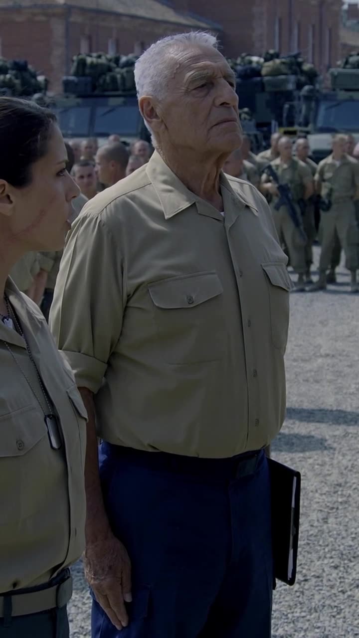 Veteran Commander Philippe stands rigidly at attention beside Camille in front of gathered troops.