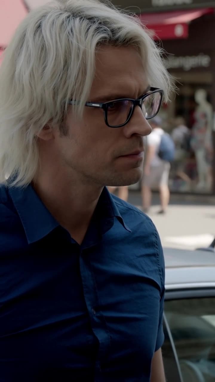 Close-up of Julien fixing Damien with a calm, steely glare through his dark-rimmed glasses.
