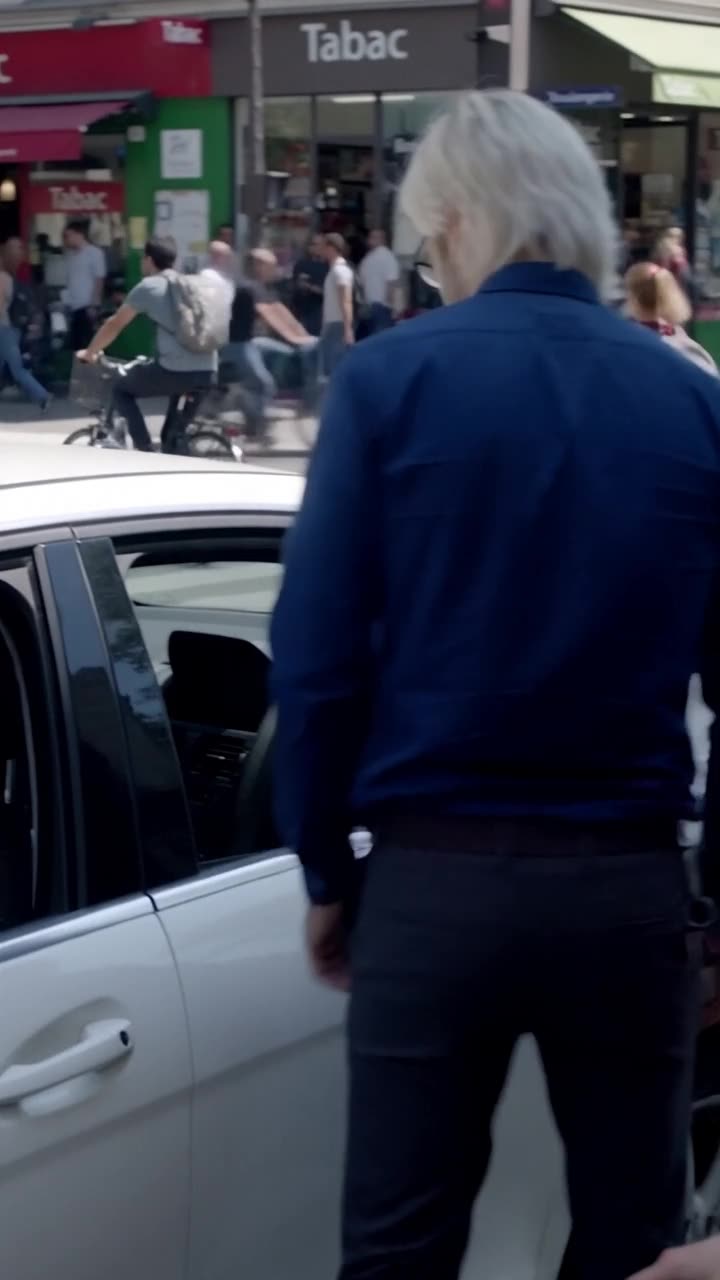 Julien turns toward the white car as an intruder darts into the driver seat.