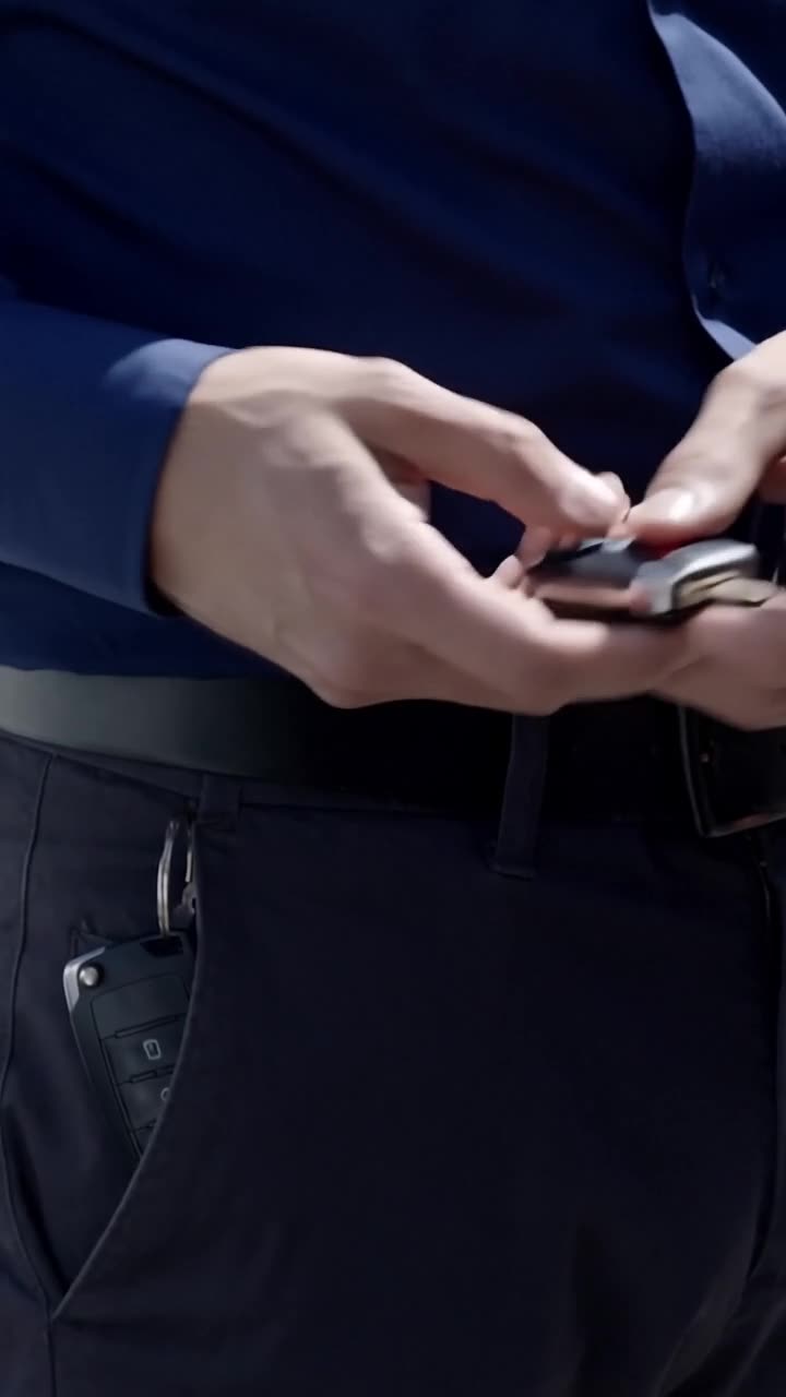 Close-up of hands unclipping an electronic car key fob from a belt loop beside a smartphone.