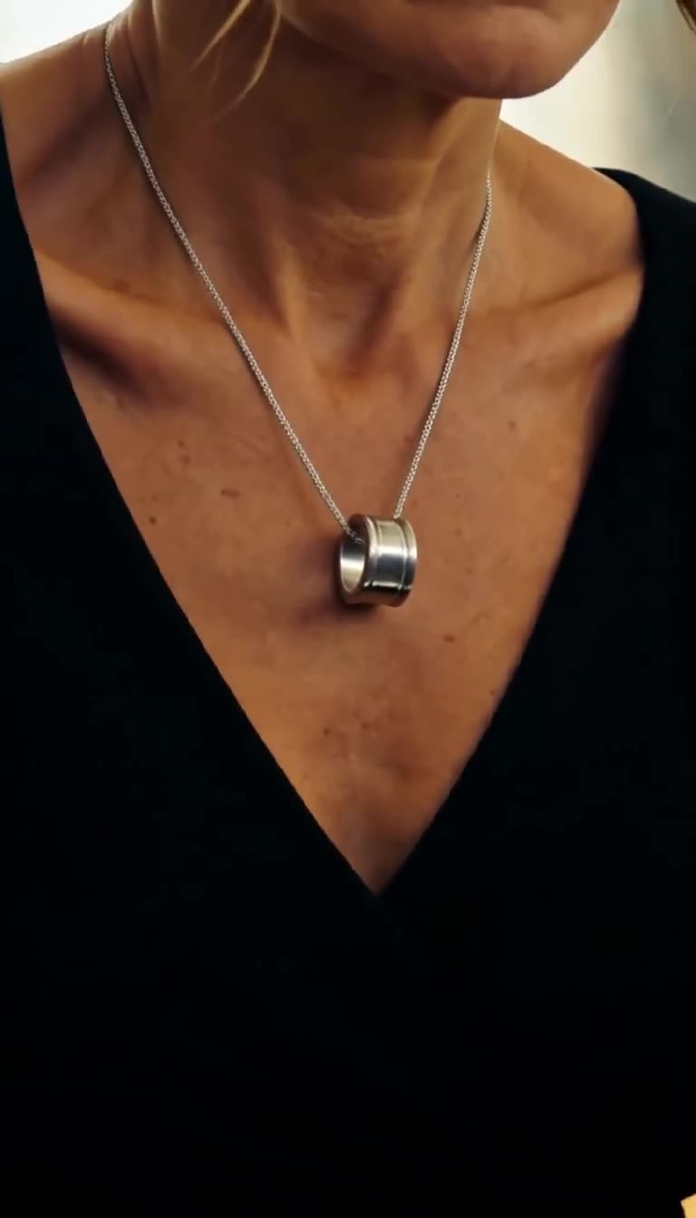 Camille reveals a thick silver signet ring hanging on a chain against her black dress