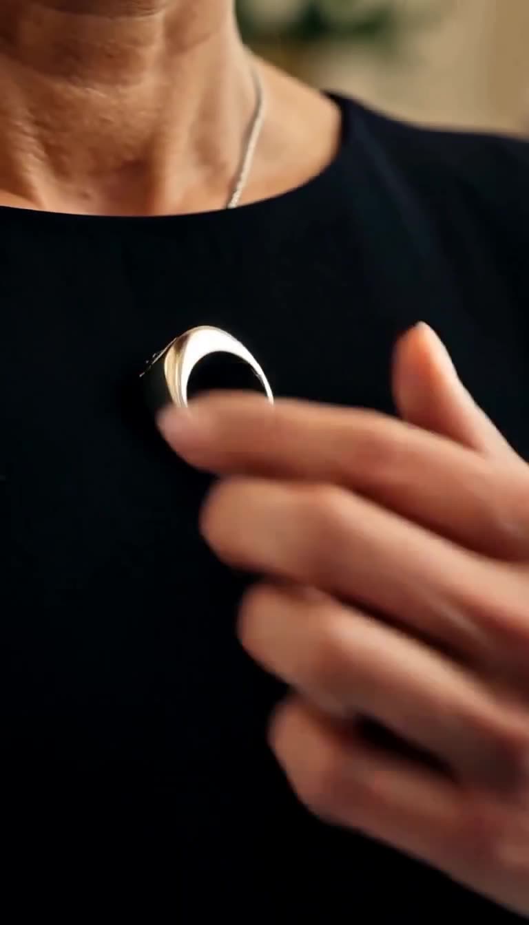 Extreme close-up of Camille's hand touching the silver signet ring resting against her black dress.