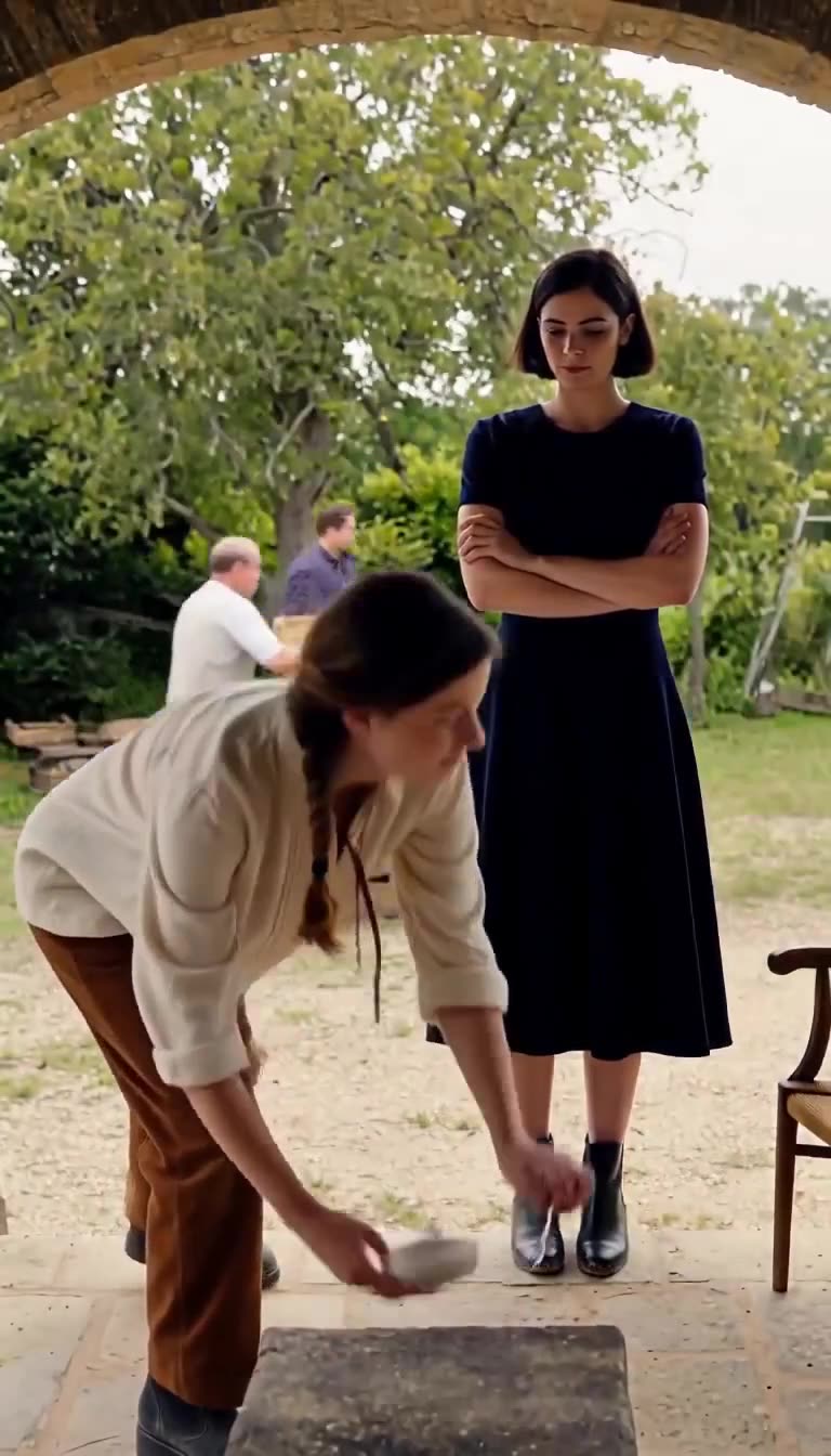 Juliette places a bowl on the ground as Constance stands over her with arms crossed