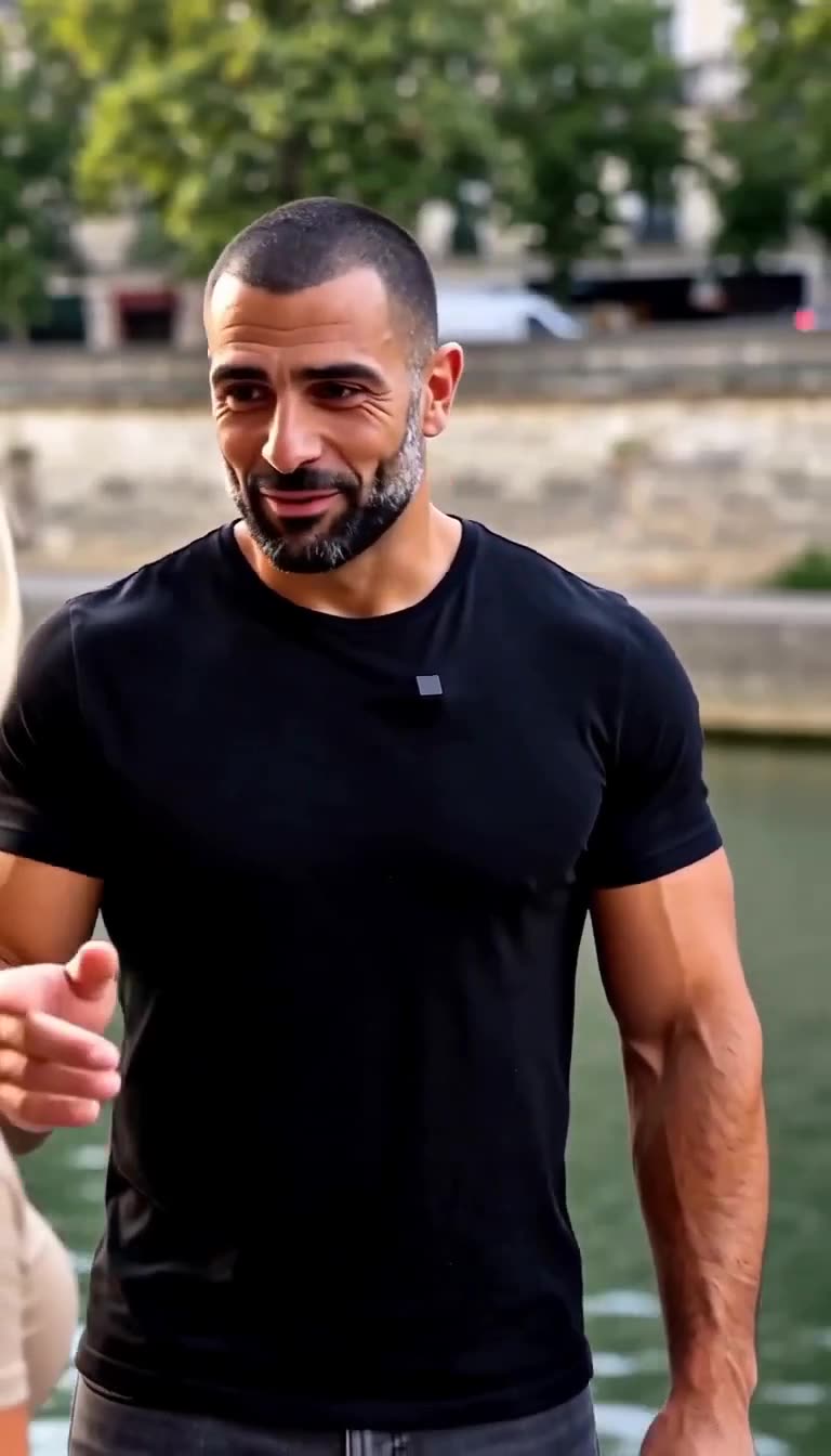A close-up of a bearded man in a black t-shirt standing beside the canal embankment