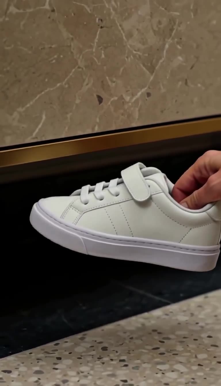Close-up of Camille's hand retrieving the small white toddler sneaker from beneath the apartment furniture