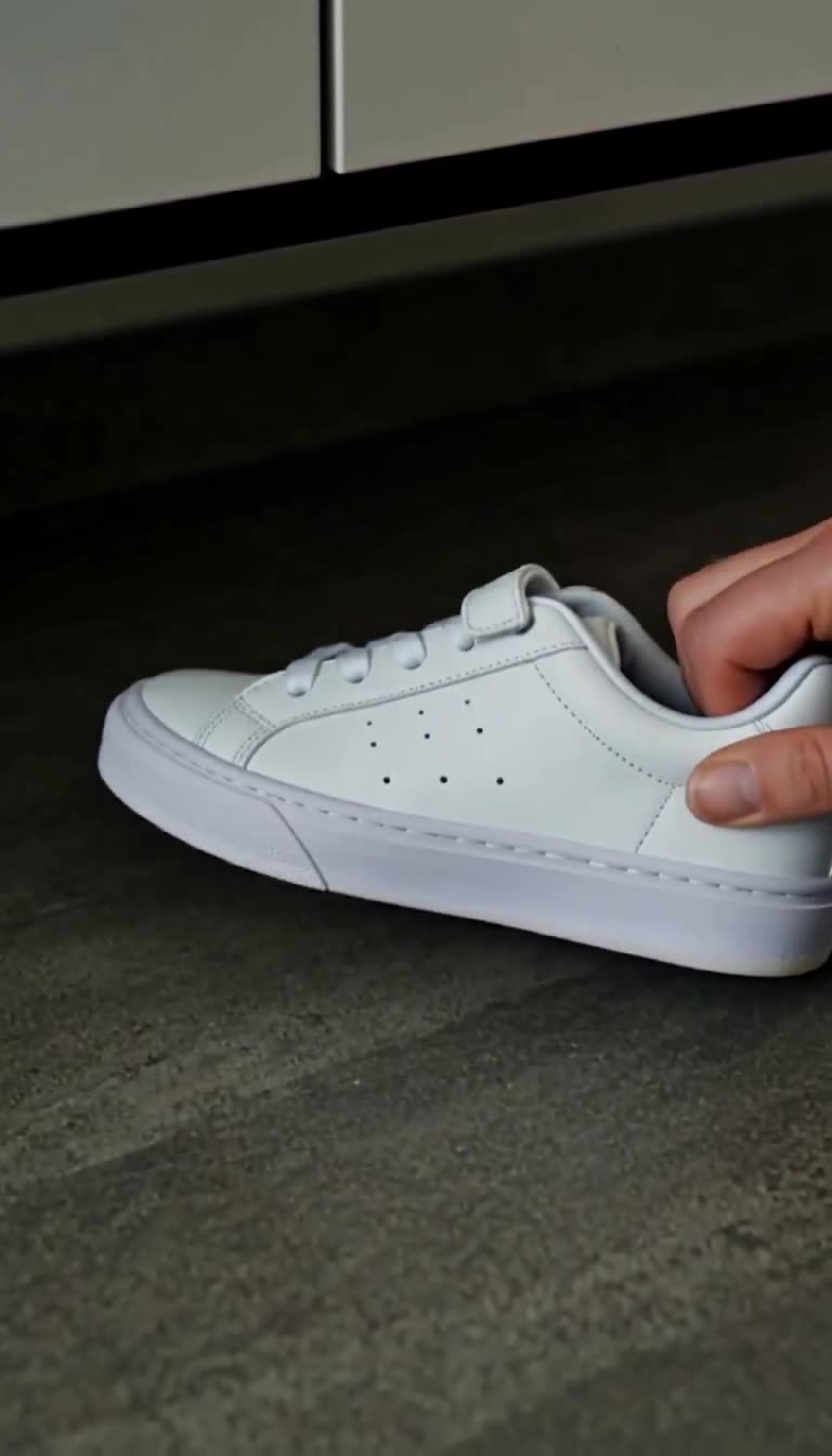 Nahaufnahme einer Hand, die einen kleinen weißen Turnschuh unter einem Schrank hervorholt.